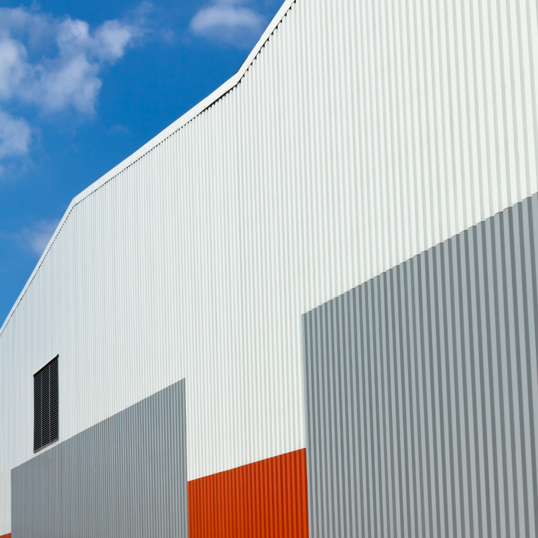 Modern architectural building with white, gray, and orange corrugated panels under a clear blue sky.